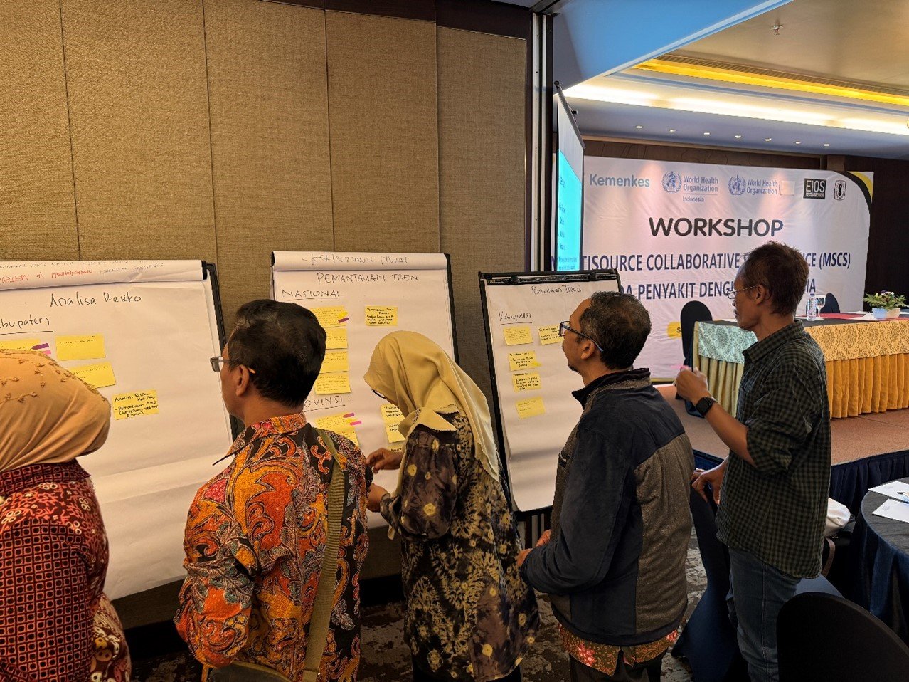 Several people are standing in front of large sheets of paper on easels, discussing and writing notes